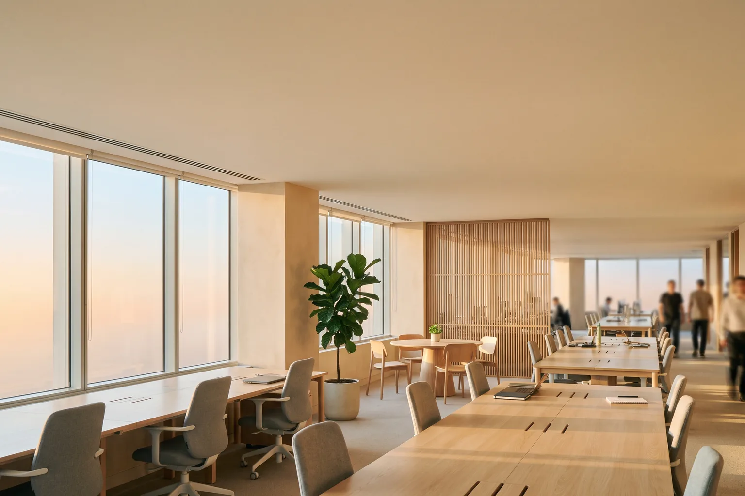An open-plan office floor at blue hour, the city skyline through the glass
